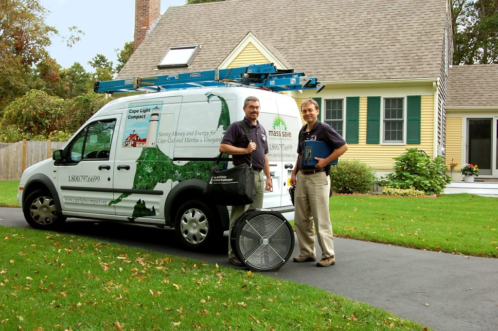 two men standing outside cape light compact van with yellow house in background